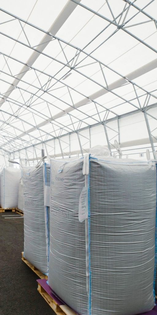White bulk bags on wooden pallets in a bright warehouse with an exposed steel framework.